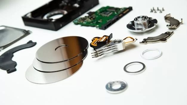 Dysk twardy rozłożony na części: obudowa, talerze, głowice, płytka elektroniki, silnik